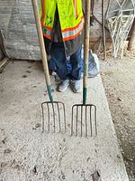 Two long wood-handled garden forks with metal tines on concrete floor