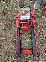 Full view of red hydraulic motorcycle jack showing lift arms, foot pedal, and wheels