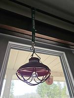 Overall view of red metal cage pendant light hanging by chain with bulb inside