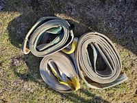 Three rolled beige nylon tow straps on ground showing loop ends