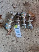 Four chrome-plated trailer hitch balls with nuts and washers on concrete surface