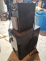 Subwoofer cube with satellite speaker stacked on top showing size and attached cords