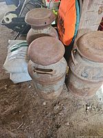 Two of three rusted steel milk cans with lids and side handles visible on barn floor