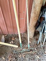 Two wooden-handle metal landscape rakes leaning against wall