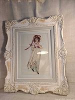 Front view of framed embroidered artwork in ornate distressed white frame