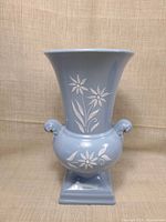 Front view showing light blue porcelain vase, white floral decoration, handles, pedestal base