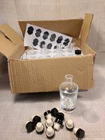 Box holding glass bottles in foam tray, caps, funnel and label sheet visible