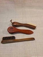 Three wooden shoe brushes displayed on fabric
