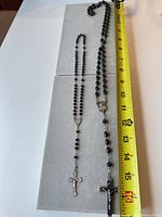 Two black rosaries laid out beside tape for length reference