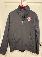 Front view of black 49ers softshell jacket hanging