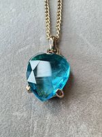 close-up of blue heart glass pendant in gold-tone setting on chain