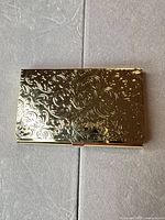 Closed gold-tone card holder showing embossed swirl pattern