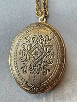 Front view of closed oval locket showing engraved floral design and attached rope chain