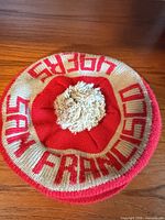 Top view showing cream pom-pom and red SAN FRANCISCO lettering on cream band