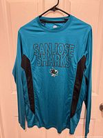 Front view of teal San Jose Sharks long-sleeve jersey on hanger