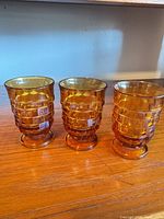 Front view of three amber pressed glass footed tumblers
