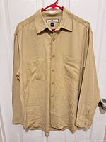 Front view of tan silk shirt on hanger showing overall style, pockets, buttons