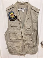 Front view of Trail Designs tan cotton canvas utility vest hanging on door