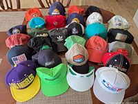 Overview of approximately 25 multicolor adjustable caps and visors spread on table