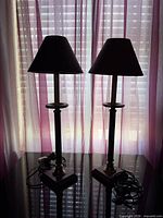 Pair of burgundy table lamps on glass surface, window backdrop