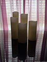Five ivory flameless LED candles standing on reflective surface against window