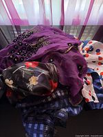Pile of assorted scarves showing embroidered purple scarf, polka-dot scarf, floral print scarf and plaid scarf