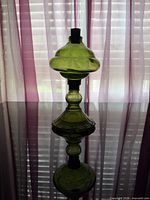 Full view of green glass oil lamp standing on reflective surface