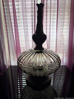 Full lamp silhouette against window showing glass body and metal neck