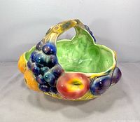 Three-quarter view showing handle, interior green glaze and fruit relief