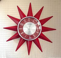 Full view of red starburst wall clock on wall