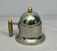 Front view of stainless sugar bowl showing brass handle and knob