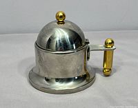 Front view of stainless steel sugar bowl showing brass handle and top finial