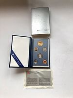Closed silver outer box above open blue case showing six coins and certificate