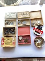 Overall view of seven boxes and two tins showing variety of watch parts and branded packaging