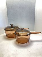 Both amber glass saucepans with lids side by side