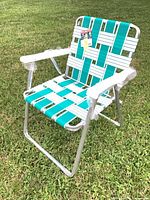 Full view of folding lawn chair on grass showing frame, webbing pattern, armrests and tags