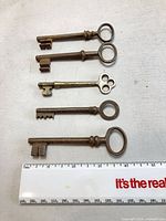 Five brass skeleton keys aligned beside ruler showing 3-4 inch length