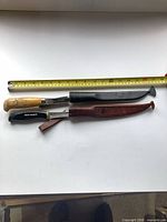 Top and bottom view of both fillet knives with sheaths and tape measure for scale