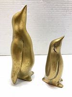 Front view of tall and small brass penguin figurines standing upright