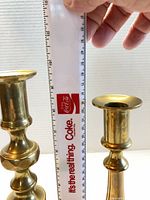Pair of brass candlesticks beside ruler showing relative heights