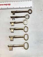 Six brass skeleton keys laid out beside ruler