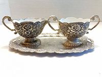 Front view of creamer and sugar bowl on tray showing floral embossing and scalloped rims
