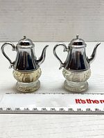 Front view of both teapot-form shakers with ruler for scale