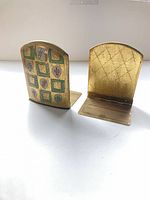 Front view showing heraldic enamel decoration on one bookend and plain brass reverse on the other