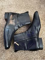 Side view of both black leather ankle boots showing uppers, side zippers and overall wear