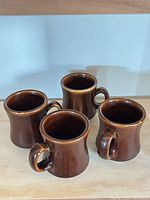 Four brown ceramic mugs grouped on surface
