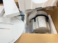 Box interior showing both Crestron Saros speakers with white grilles, black baffles, packaging foam and plastic