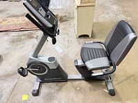 Side view of NordicTrack recumbent bike showing frame, seat, flywheel, pedal strap and branding