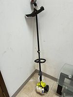 Full view of Ryobi string trimmer leaning upright showing engine housing, shaft and head