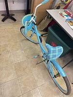 Full view of light blue step-through cruiser bicycle with basket and plaid saddle